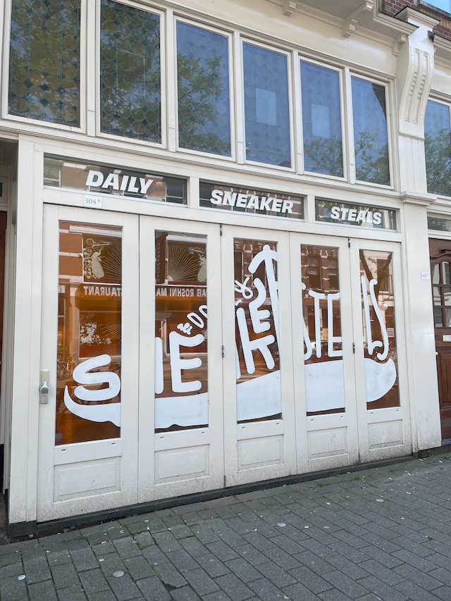 Witte pui van Daily Sneaker Steals aan de Nieuwe Binnenweg in Rotterdam met handgeschilderde belettering op de ramen